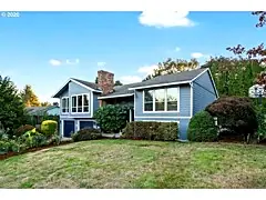 Two-story blue house exterior with lawn and mature trees