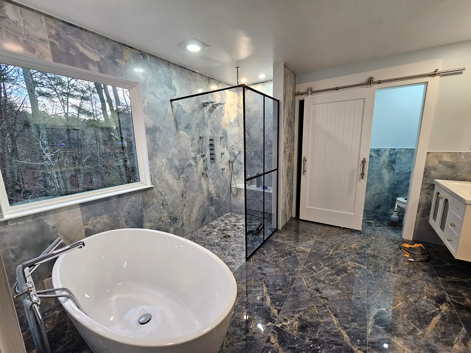 Renovated primary bathroom with walk-in glass shower, freestanding tub and marble floor — a Lion Pride project